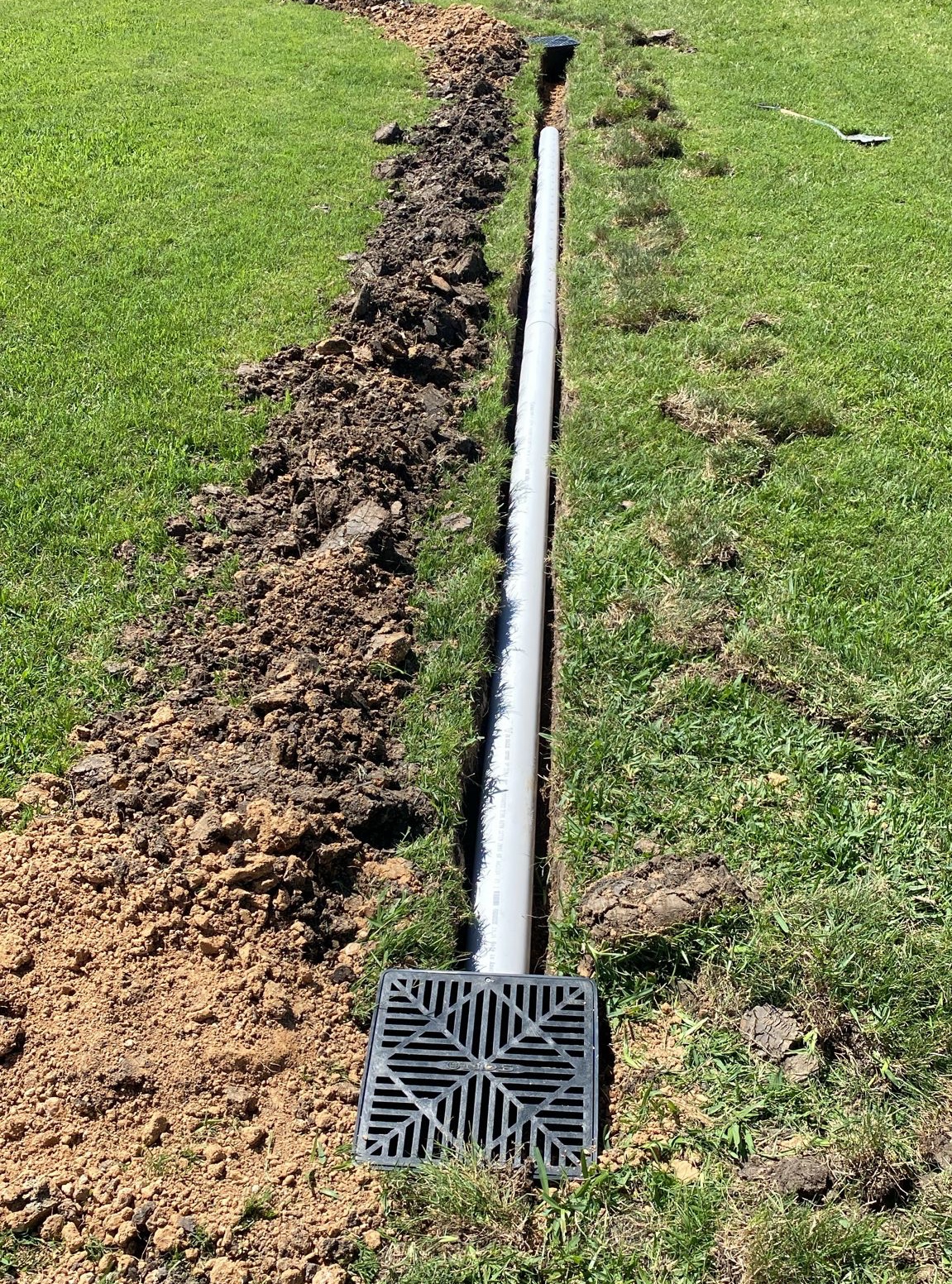 Catch basin grate with PVC drainage pipe in a freshly dug trench in Houston