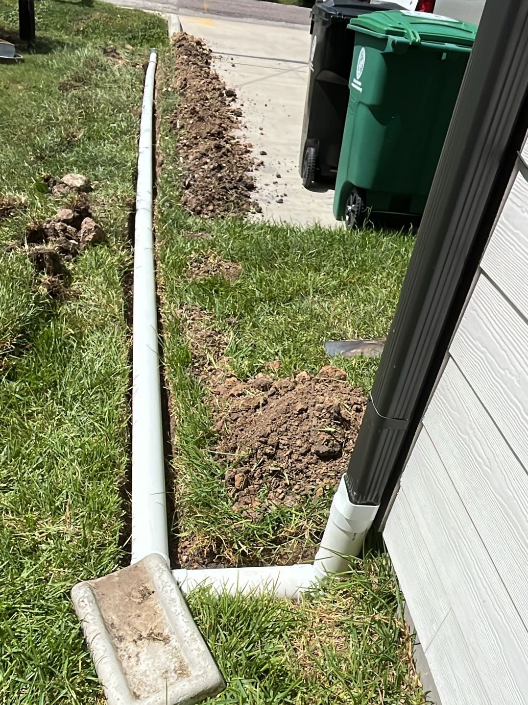 Downspout extension PVC pipe being installed along a Houston home foundation