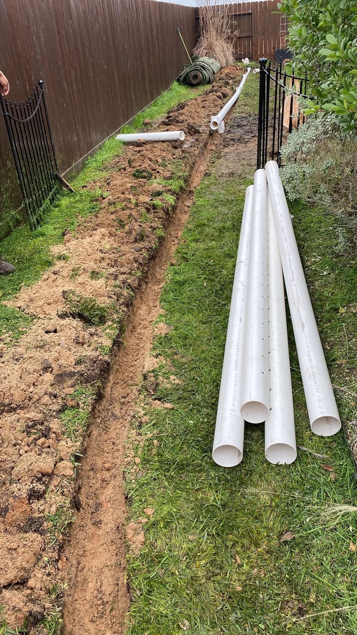 French drain installation with PVC pipes and trench in a Houston TX backyard