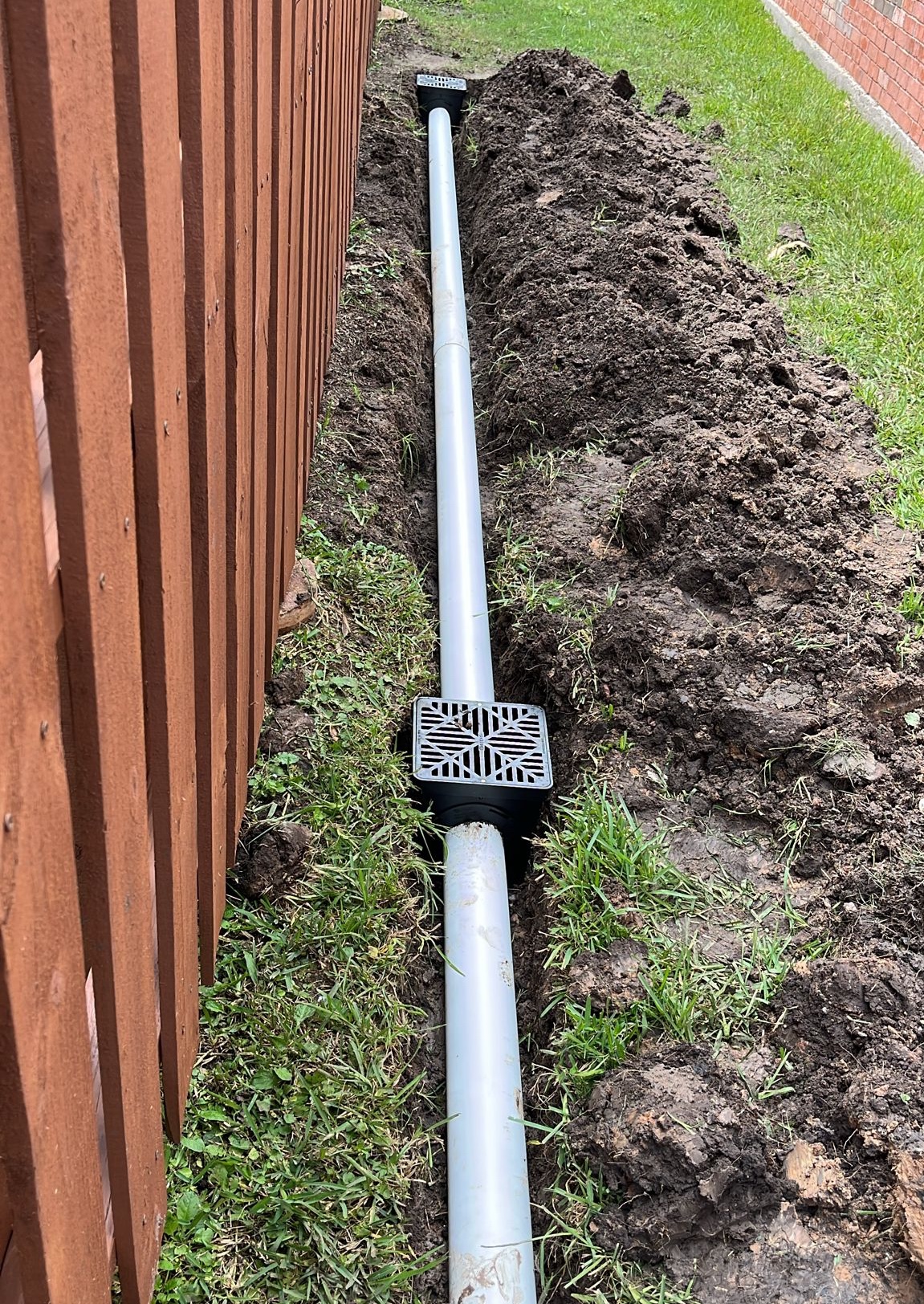 French drain PVC pipe and catch basin installed along a fence line in Houston